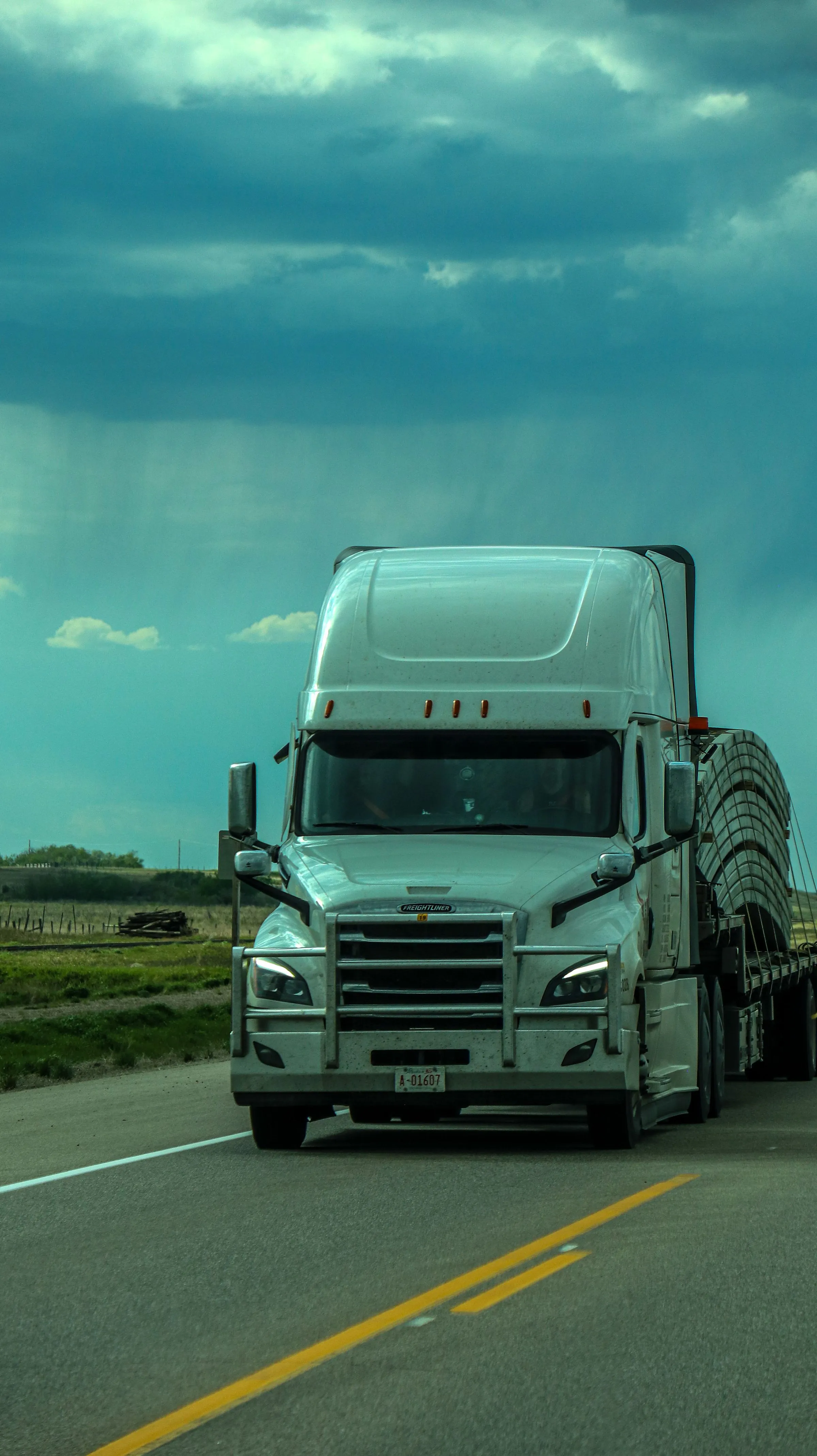 A tractor-trailer running an interstate highway under a breaking sky